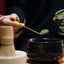 Person preparing matcha with a container of Kayo Matcha on a wooden table.