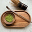 Matcha - Wooden bowl with green powder, wooden whisk, and wooden scoop on a marble surface. Chasen